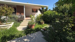 Una casa con porche cubierto, escalones que conducen a la entrada y un jardín con diversas plantas.