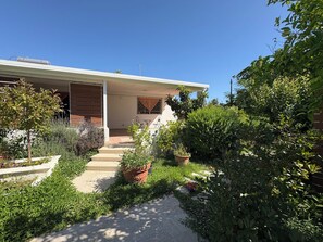 Ein Haus mit überdachter Veranda, Treppen zum Eingang und einem Garten mit verschiedenen Pflanzen.