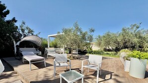 Un patio al aire libre con mobiliario, una pérgola y vistas al jardín.