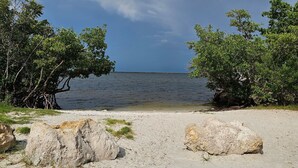 A beach with clear water, trees, and large rocks.