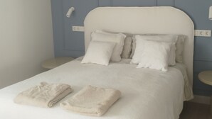 Een slaapkamer met een bed, kussens, een nachtkastje en een stopcontact.