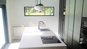 Een moderne keuken met een centraal eiland, hangende lampen en uitzicht op groen.