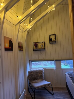 A cozy room with wooden walls, a fluffy chair, a bed, and a window with a view. - Lovely cabin near Selfoss with amazing view and horses (Sveitarfélagið Árborg)