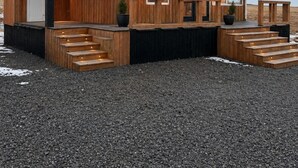 Une cabane en bois avec un porche à l’avant, des marches menant à l’entrée et une allée gravillonnée.