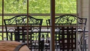 Blick durch ein Fenster mit Metallgitter, mit Gartenmöbeln und Grünpflanzen.
