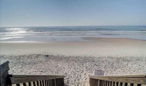 Ein Strand mit einer Holzbank und einem Schild im Vordergrund.