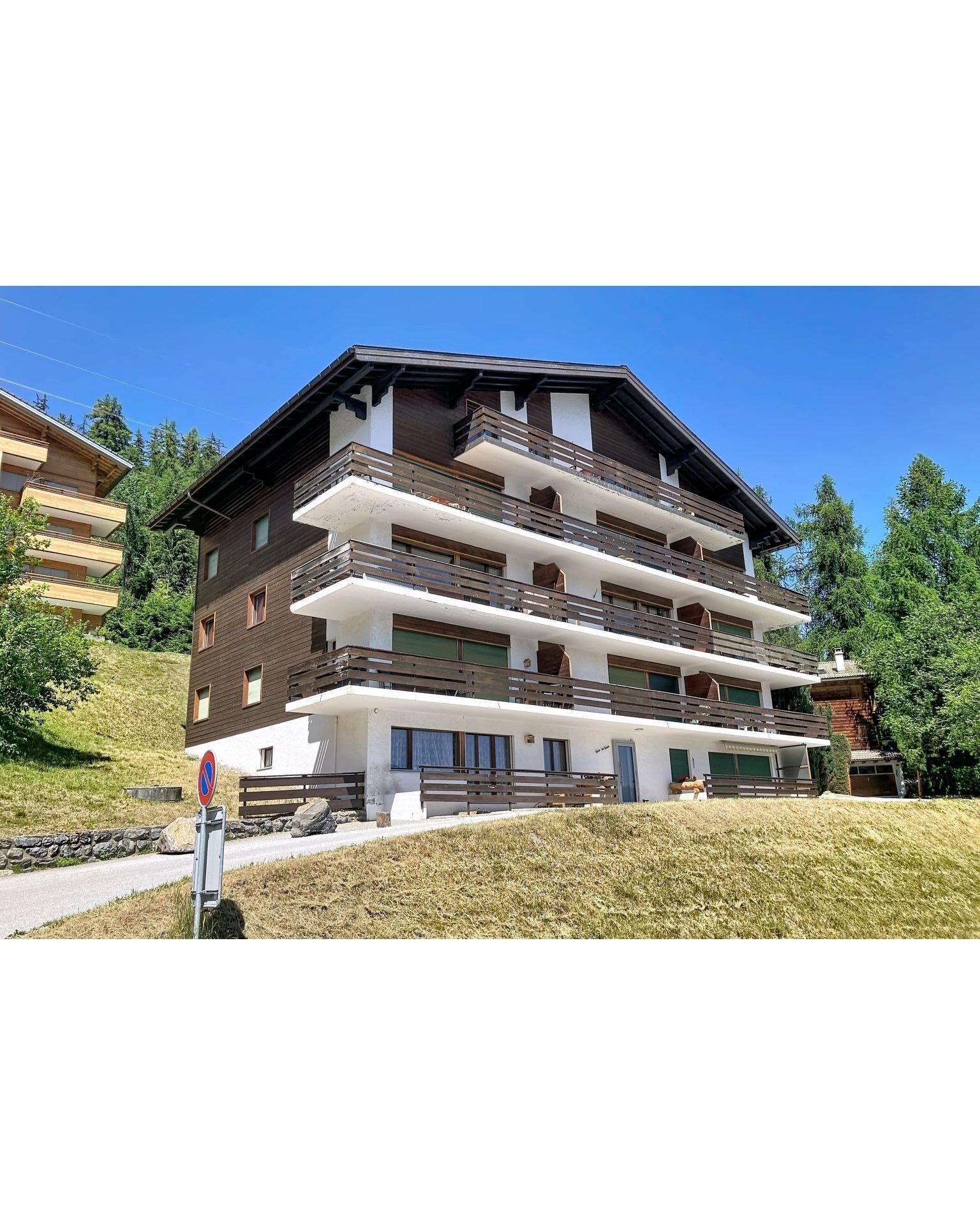 Un immeuble à plusieurs étages doté de balcons, d’un panneau indiquant qu’il est interdit de se garer et d’une zone herbeuse devant.