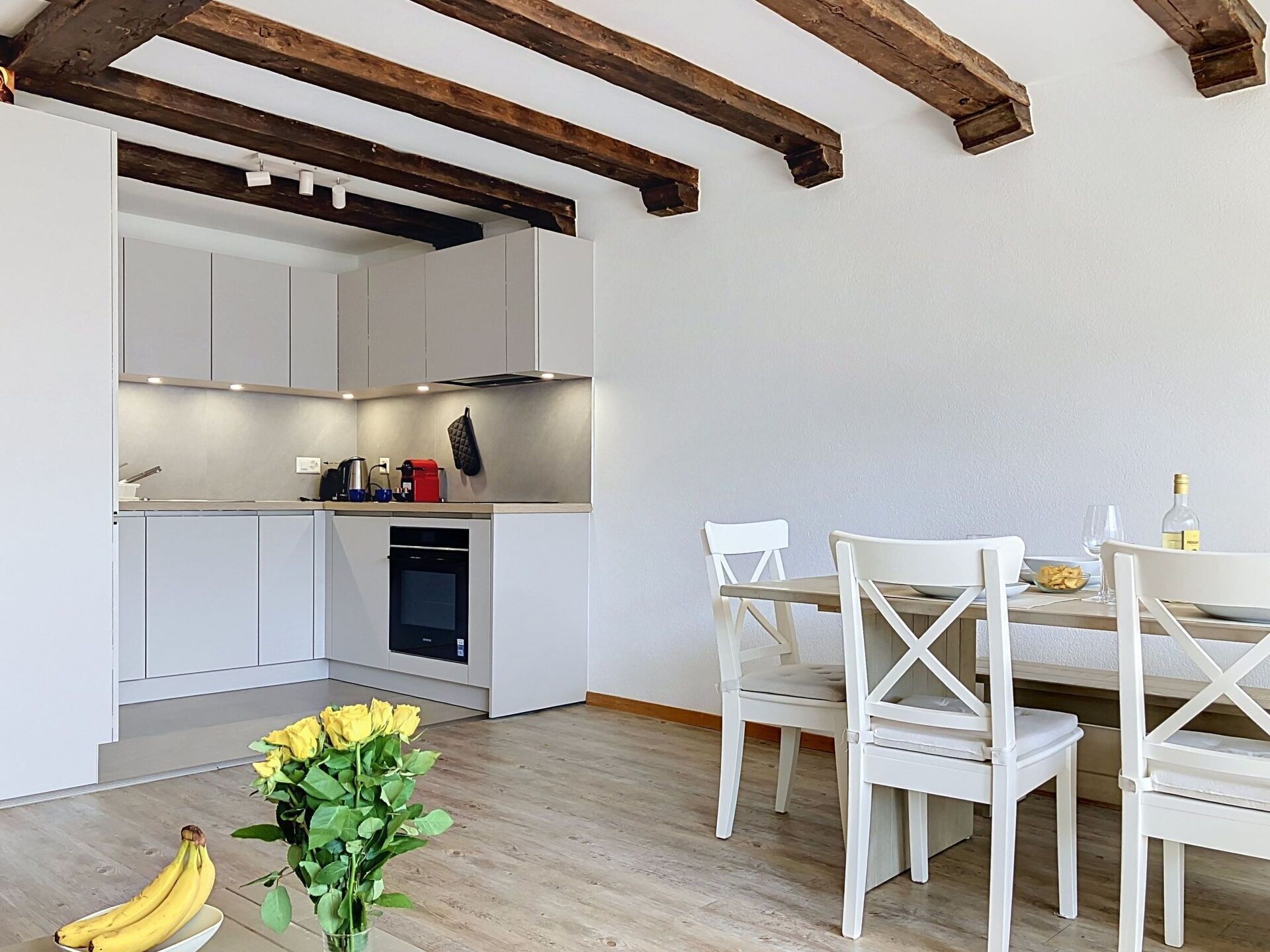 Une cuisine moderne avec des meubles blancs, une table à manger avec des chaises blanches et un plafond en bois.