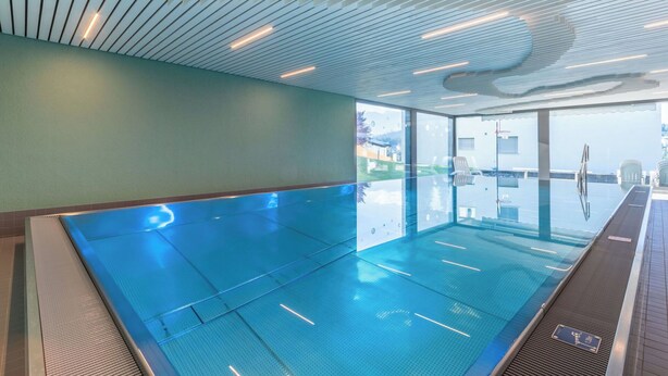 En stor inomhuspool med en modern takdesign, väggar av genomskinligt glas och utsikt mot omgivningen.