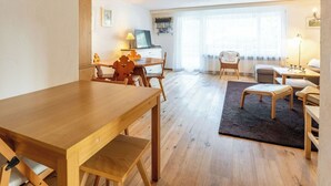 En hyggelig stue med et træbord, en sofa, et fjernsyn og et vindue med lette gardiner.