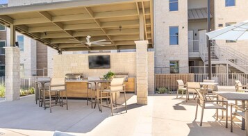 Un patio exterior con una parrilla, asientos y un televisor montado en una pared de piedra.