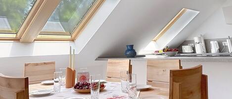 Un comedor con una mesa dispuesta para cuatro personas, un jarrón azul y un frutero.