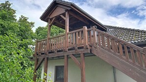 Un balcone in legno con tetto spiovente, una finestra e una ringhiera.