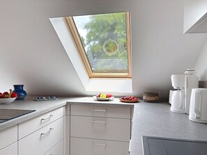 Eine moderne Küche mit Oberlicht, weißen Schränken, einer Kaffeemaschine und einer Obstschale.