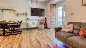 Un comedor con mesa y sillas de madera, un sofá, una guitarra y un televisor montado en la pared.