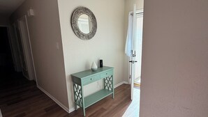 Ein Zimmer mit Holzboden, einem türkisblauen Konsolentisch mit Schubladen, einem runden Spiegel und einer Deckenleuchte.