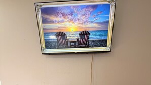 Ein an der Wand befestigter Fernseher zeigt eine Sonnenuntergangsszene, darunter ein Unterhaltungsschrank aus Holz und ein gemustertes Teppich auf dem Boden.