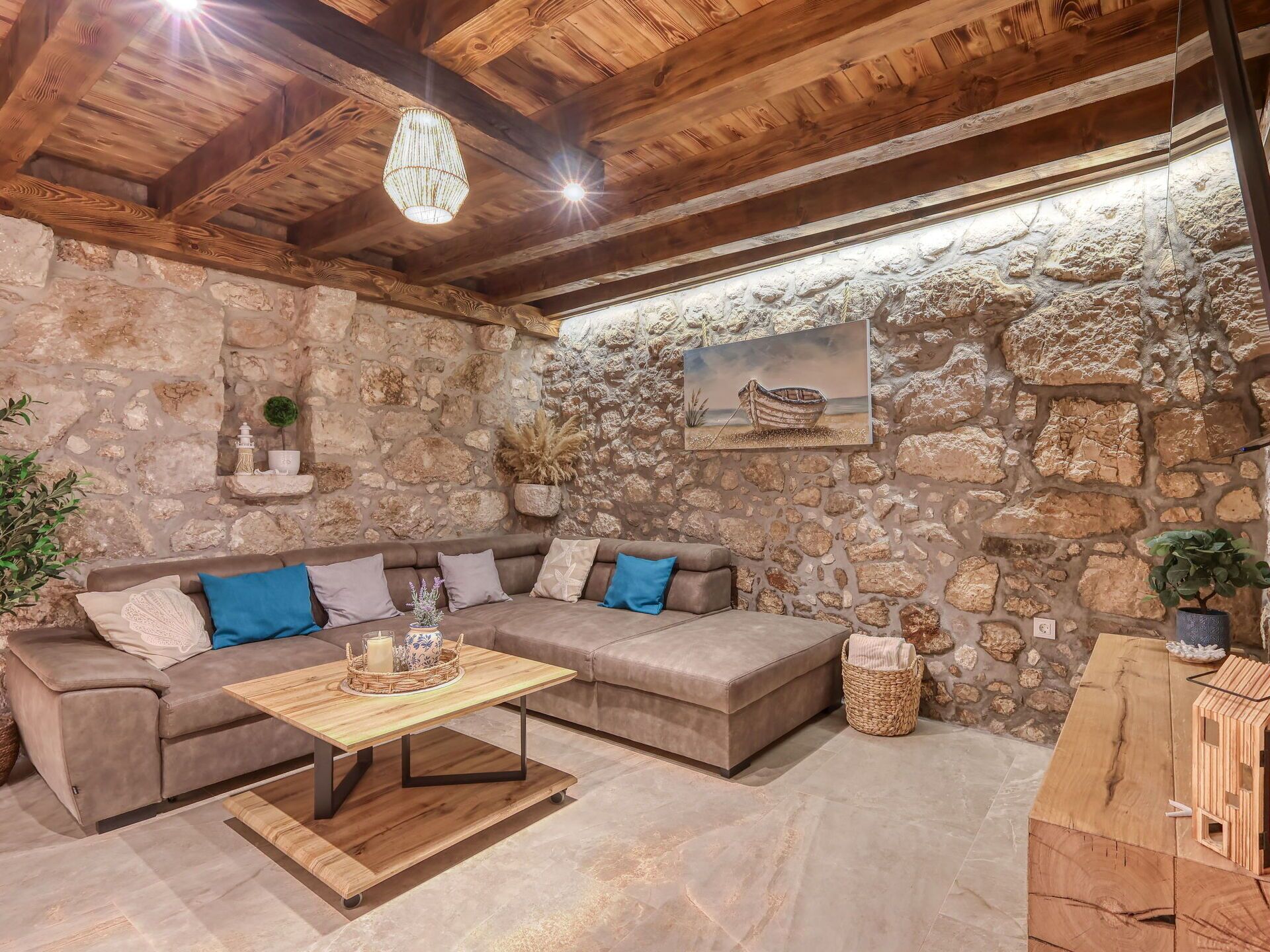 Um quarto acolhedor com parede de pedra, teto de madeira, um sofá marrom com almofadas, mesa de centro de madeira e um lustre.
