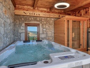 Ein Zimmer mit Steinwänden, Holzbalkendecke, einer Whirlwanne und einer Holztür mit Balkonblick.