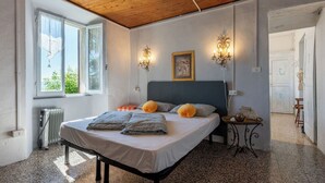A bedroom with a bed, two wall sconces, a radiator, and a window.