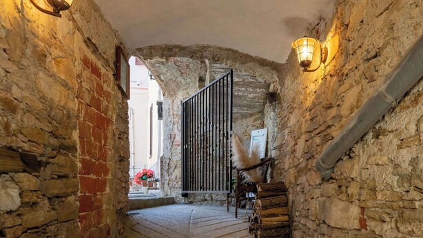 A narrow stone corridor with a wooden door, stone walls, and a tiled floor.
