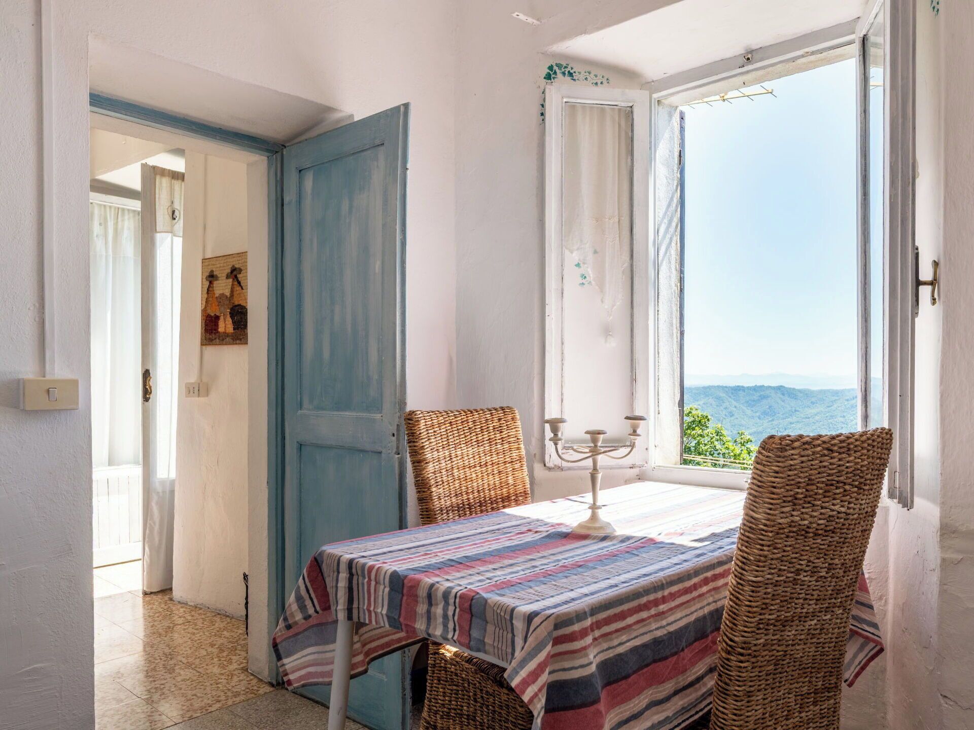 Quarto com uma mesa posta para dois, vista para o exterior e uma porta que dá para outro cômodo.