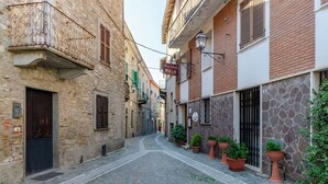 A narrow cobblestone street with stone buildings, a sign for 'MALO,' and a pedestrian crossing.