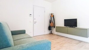 Una habitación con sofá, televisor, perchero y puerta.