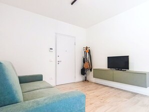 Ein Zimmer mit einer Couch, einem Fernseher, einem Kleiderhaken und einer Tür.