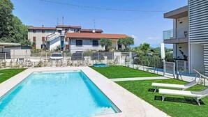 Una piscina con solárium, césped y un edificio con balcones.