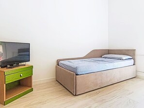 Ein kleines Schlafzimmer mit einem Bett, einem Fernseher auf einem Holzboden und einer grünen Kommode.