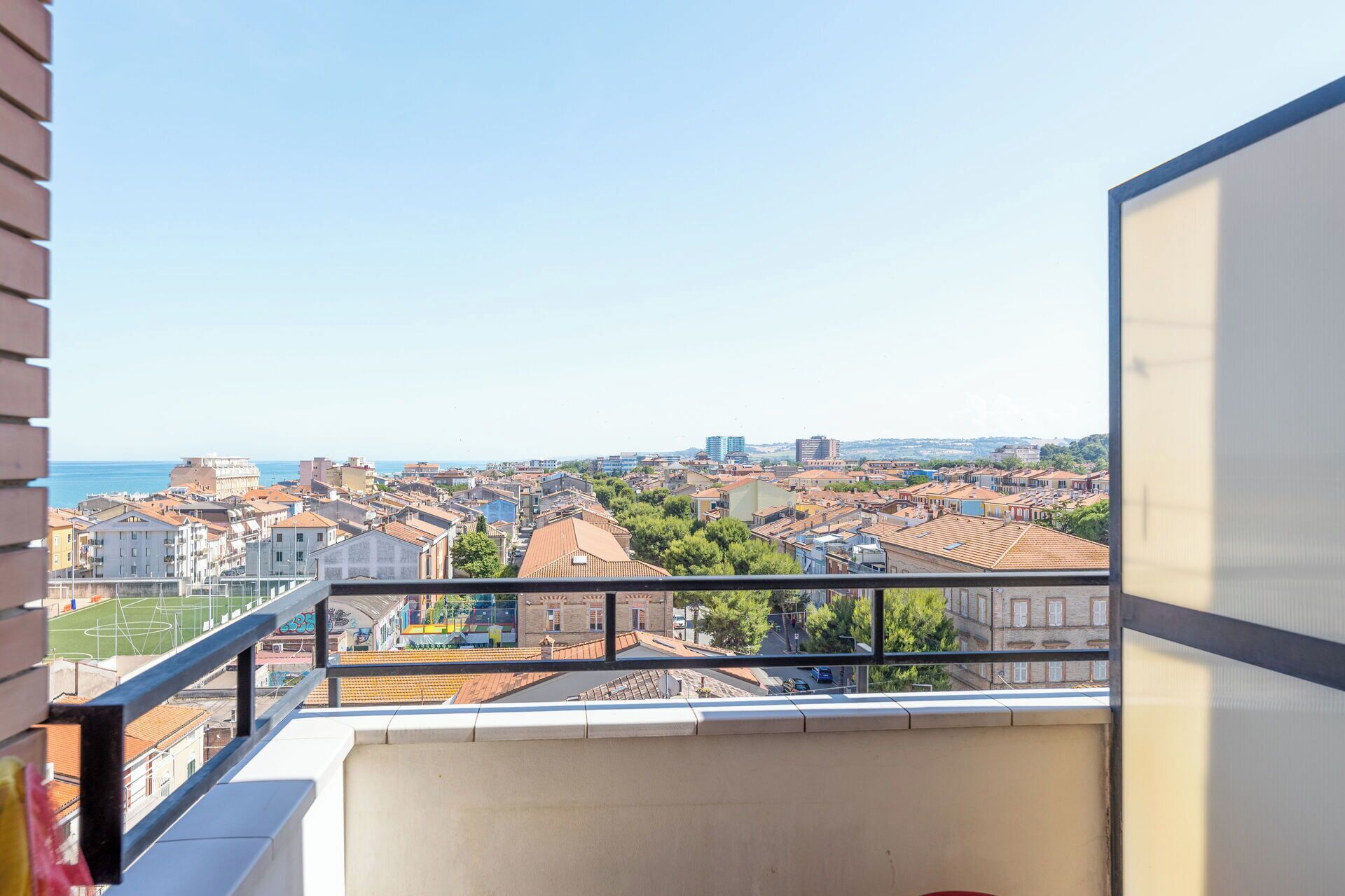 Un balcon offrant une vue sur un paysage urbain côtier, avec des bâtiments et un ciel dégagé.
