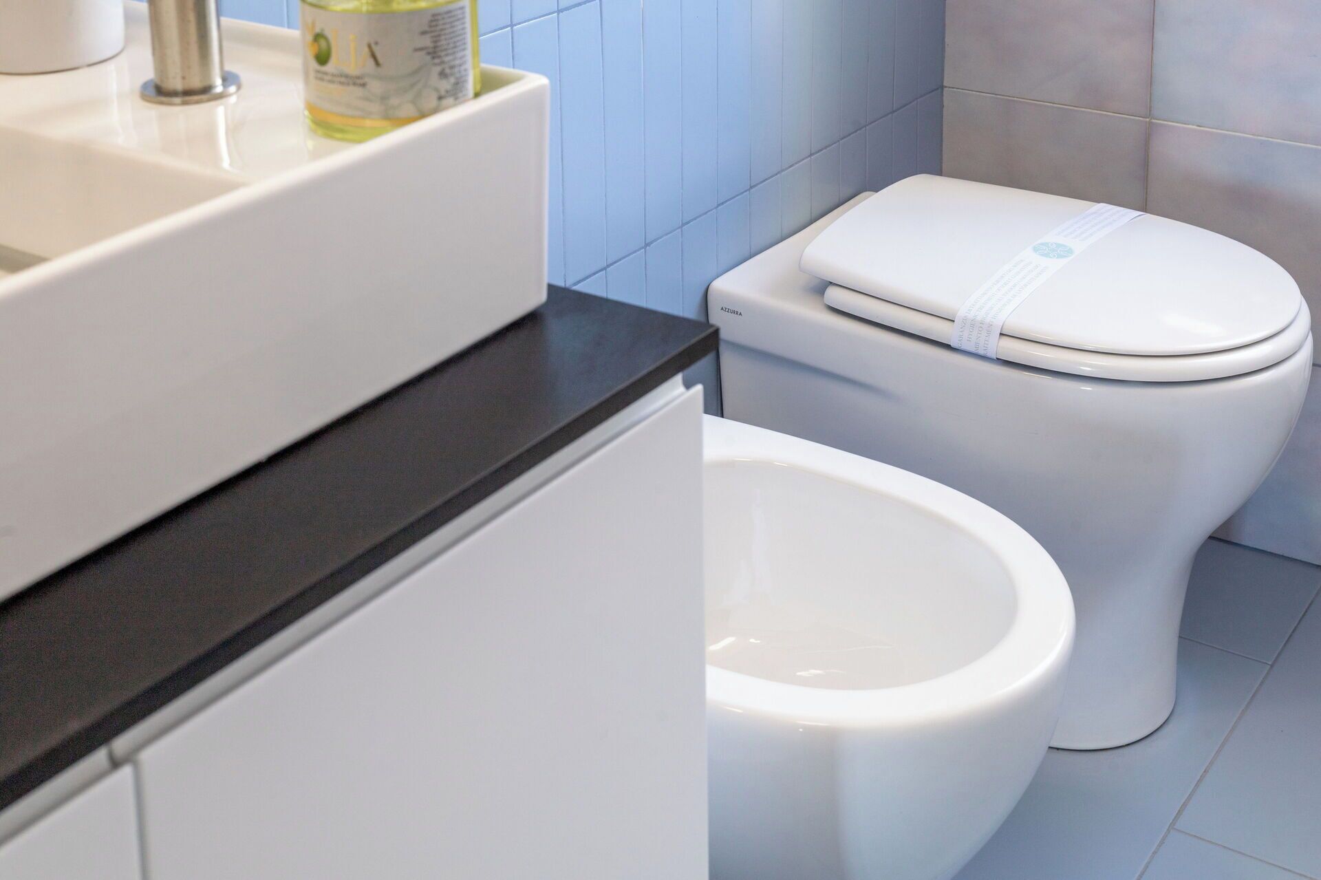 A bathroom with a white toilet, a bidet, and a sink with a bottle of lotion.