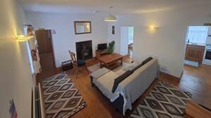 Ein Wohnzimmer mit Kamin, einer Couch, einem Esstisch und einem durch eine offene Tür einsehbarer Küchenbereich.