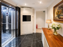 Un hall de hotel con piso de mármol, una recepción, un cuadro y un extintor.