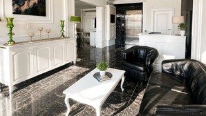 A spacious living area with a white coffee table, black leather sofa, and a dining area with a white cabinet and a green lamp. - Sahil Panorama Otel (Yomra)