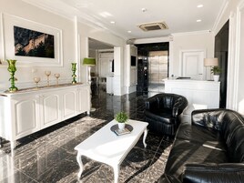 A spacious living area with a white coffee table, black leather sofa, and a dining area with a white cabinet and a green lamp.