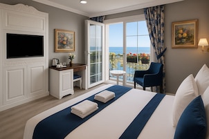 Habitación de hotel con cama, escritorio, televisión, balcón con vistas y una silla.