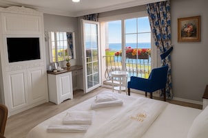 Un cuarto de hotel con cama, televisor, escritorio, silla, balcón con vistas y un cuadro en la pared.