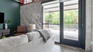Quarto com sofá, poltrona, luminária e vista para o verde através de uma porta de vidro.