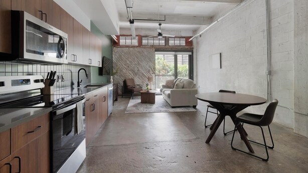 Uma cozinha moderna com forno embutido, um espaço de refeições com mesa redonda e cadeiras, e uma sala de estar com sofá e parede estampada.
