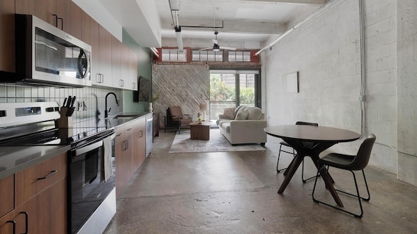 A modern kitchen with a built-in oven, a dining area with a round table and chairs, and a living space with a sofa and a patterned wall. - Landing Chic 1bd, Gym, Rooftop Lounge (Jacksonville)