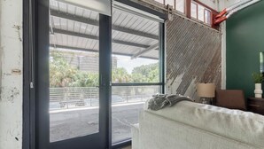 Quarto com porta de correr de vidro que dá para área externa, sofá, luminária e pequena mesa com uma planta.