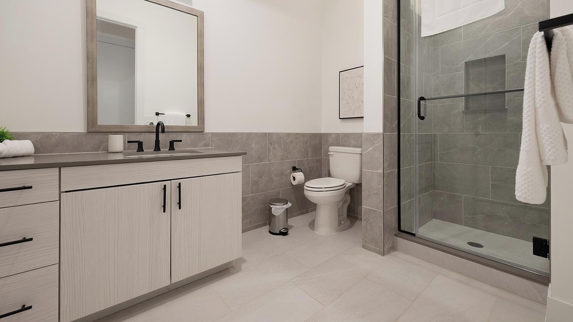 A modern bathroom with a glass shower enclosure, a toilet, and a sink with a mirror above.