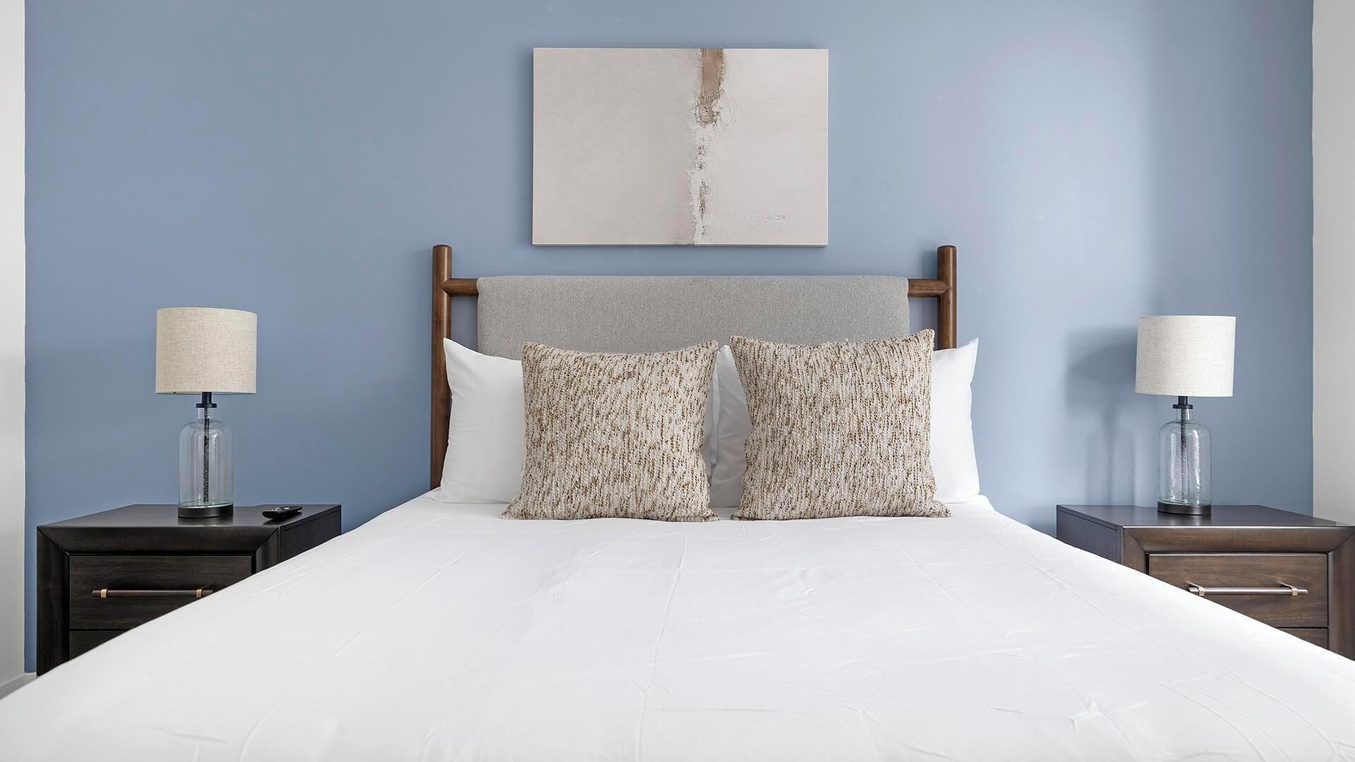 A bed with white bedding, two matching pillows, a wooden headboard, and two bedside tables with lamps.