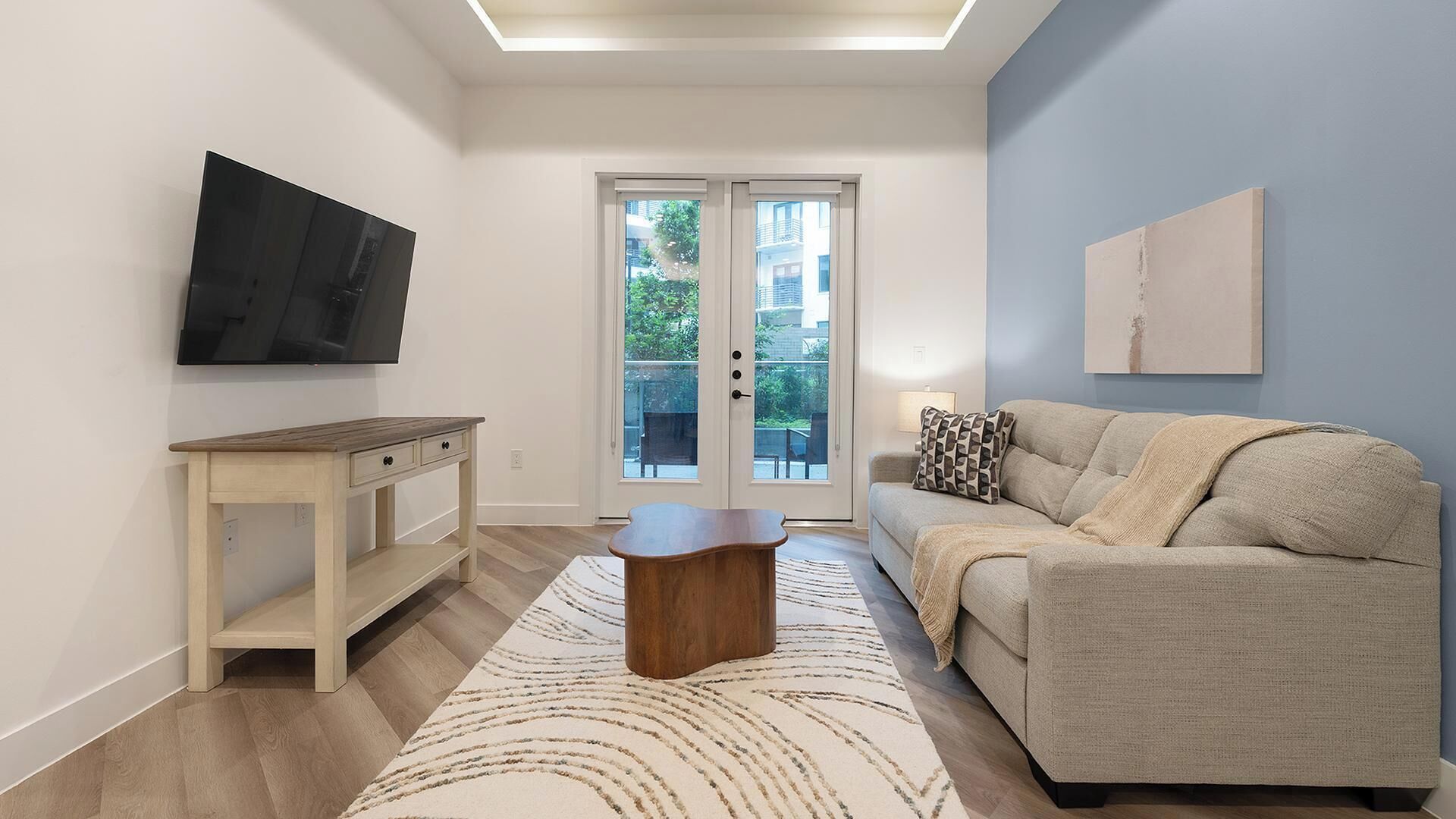 A modern living room with a flat-screen TV, a wooden coffee table, a sofa, and a patterned rug.