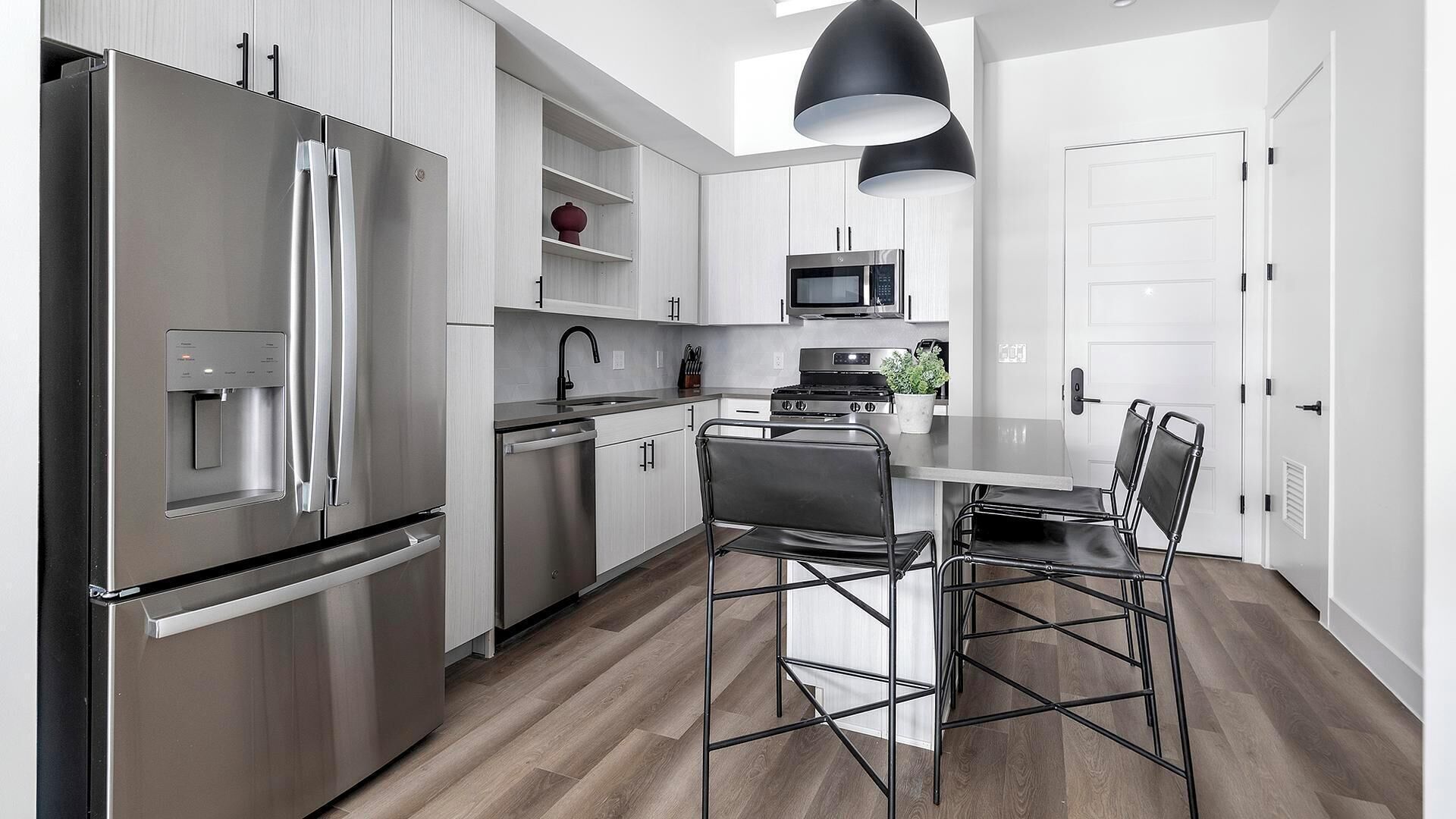 A modern kitchen with stainless steel appliances, a water dispenser, a microwave, and a dining area with metal chairs.