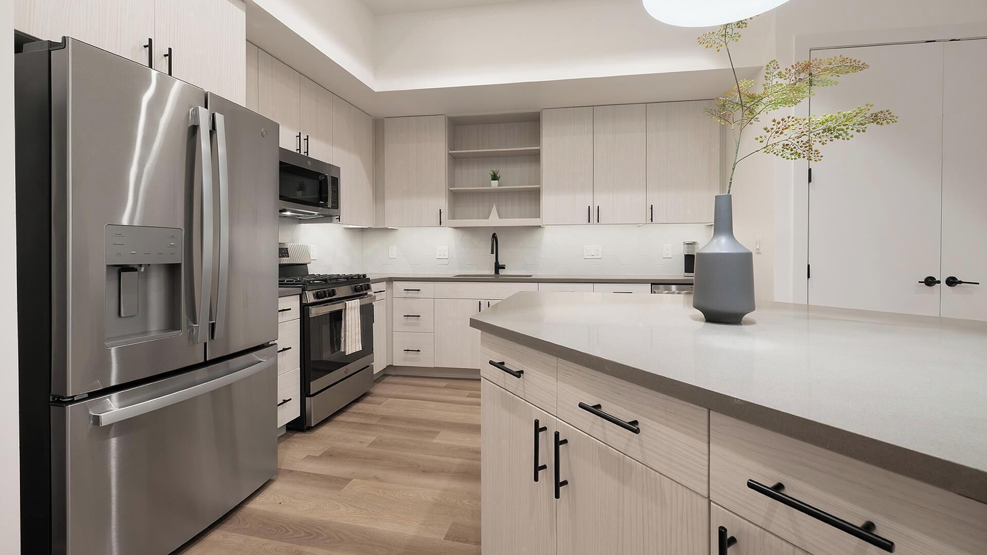 A modern kitchen with stainless steel appliances, light wood cabinetry, and a central island.