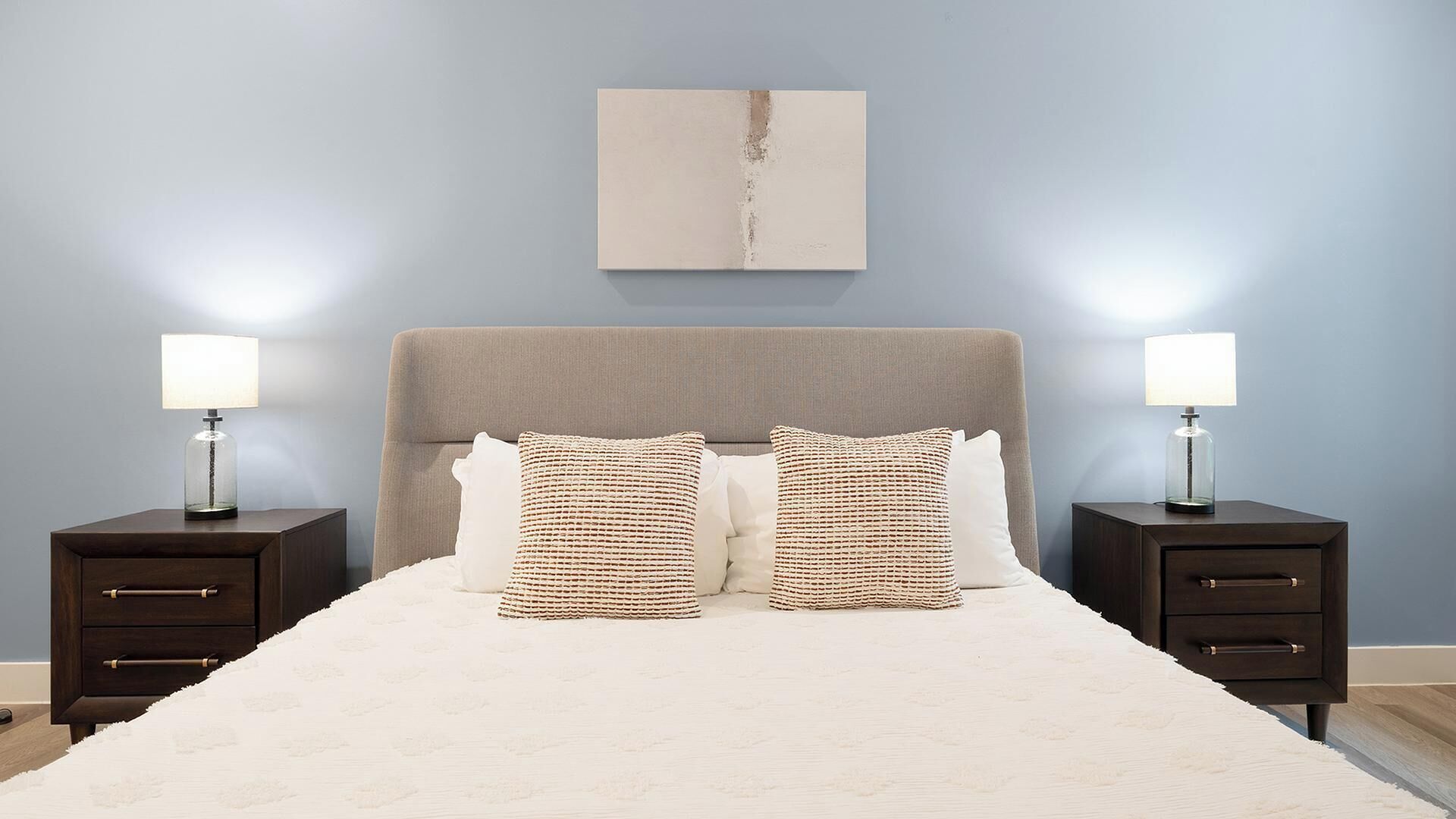 Un dormitorio con una cama, dos mesitas de noche, un cabecero y una obra de arte colgada en la pared.