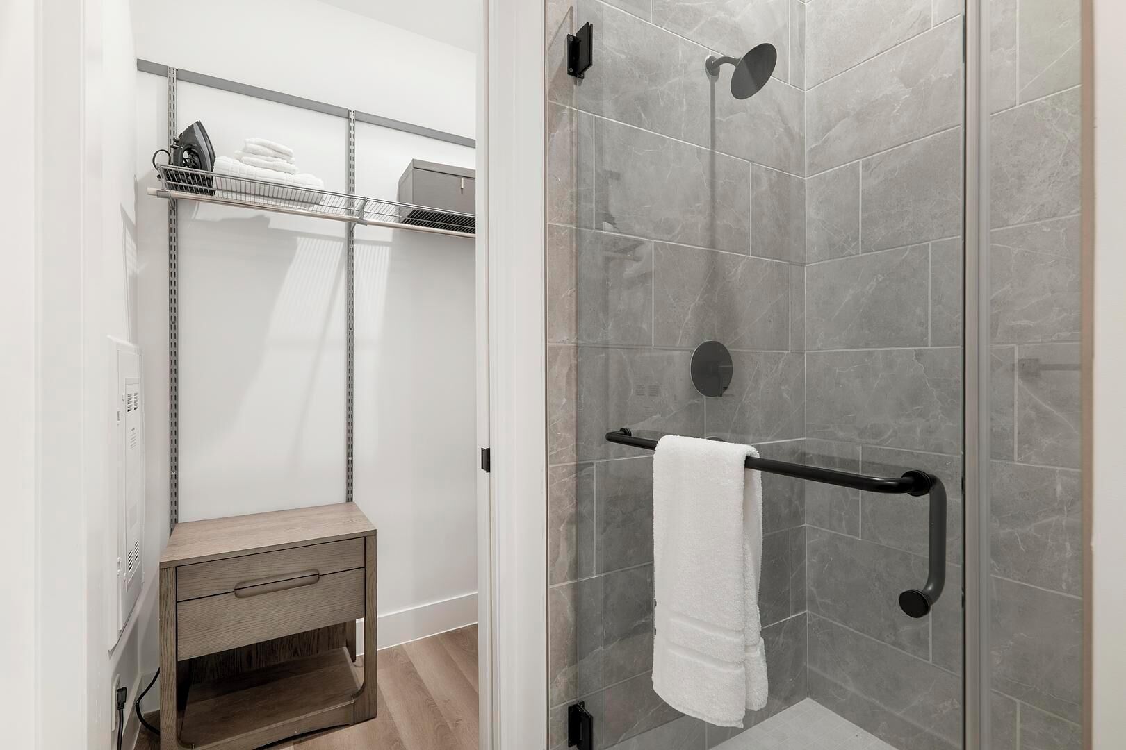 Una ducha con puerta de vidrio, un perchero y un tocador de madera con un cajón.